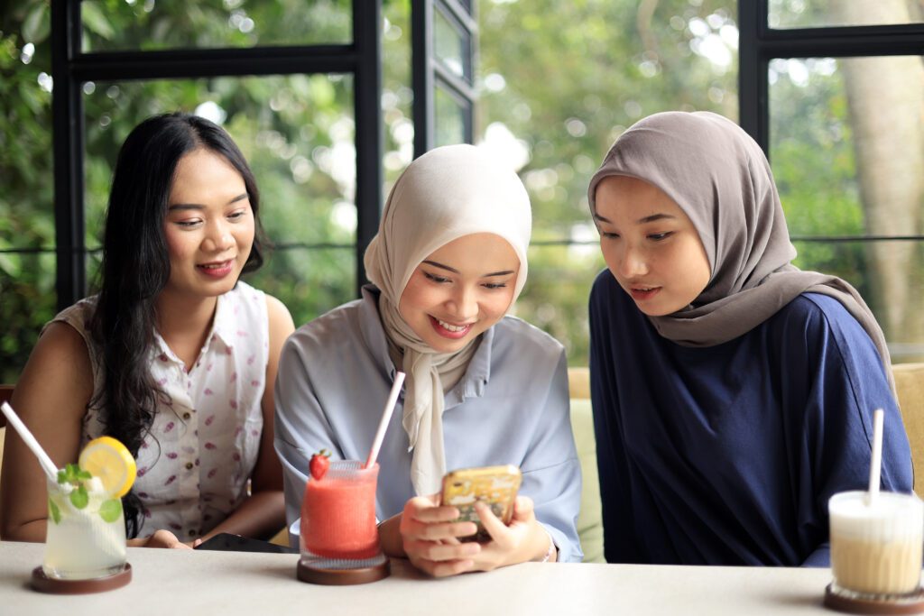 Group of Cheerful and Pretty Asian Female Friends are Enjoying a Coffeeshop While Travelling, Looking at Mobile Phone